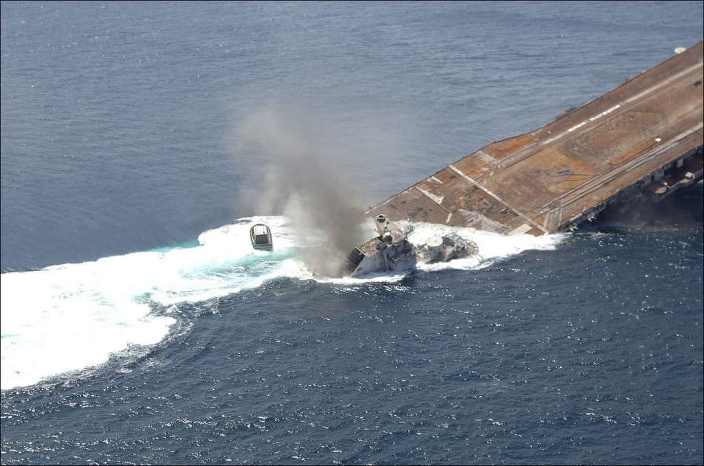 USS Oriskany sinking at a steep angle with foam and smoke at the waterline