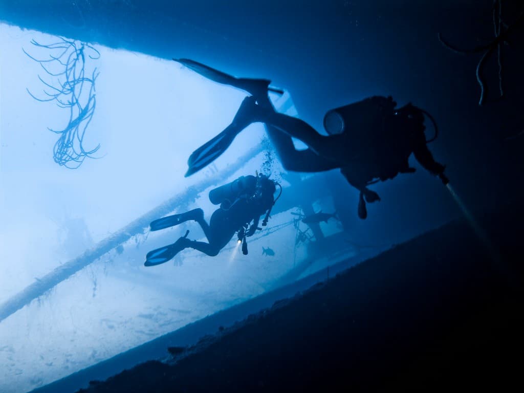 Divers silhouetted in a wreck hatch